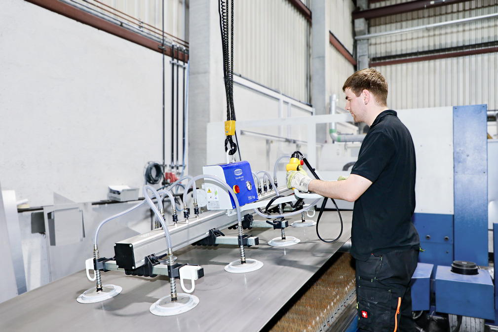 The employee places the large-format sheet on the feed unit of the laser cutting system with the help of the vacuum lifting device VacuMaster.